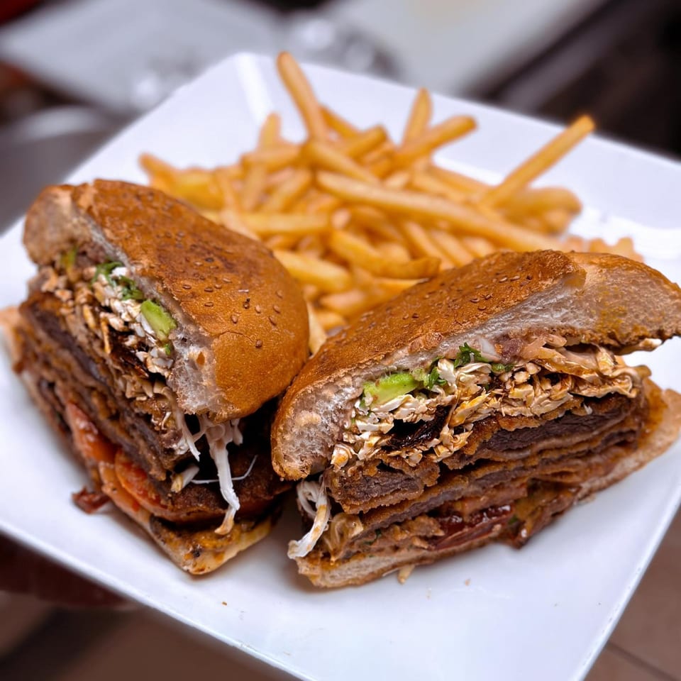 A large, sliced sandwich filled with meat, cheese, and vegetables, served with a side of fries.