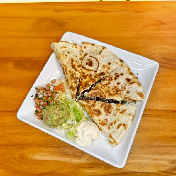 A quesadilla cut into four triangles, served with guacamole, pico de gallo, and sour cream.