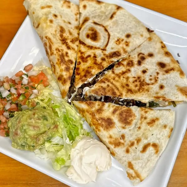 A large quesadilla cut into four triangles, served with guacamole, pico de gallo, lettuce, and sour cream.