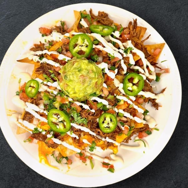 Nachos topped with shredded beef, melted cheese, pico de gallo, guacamole, sour cream, and jalapeños.